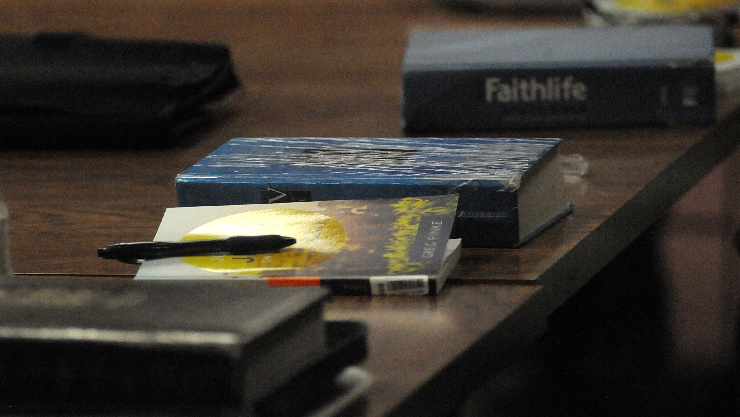 A new Christian book and a worn bible on a table with a pen.